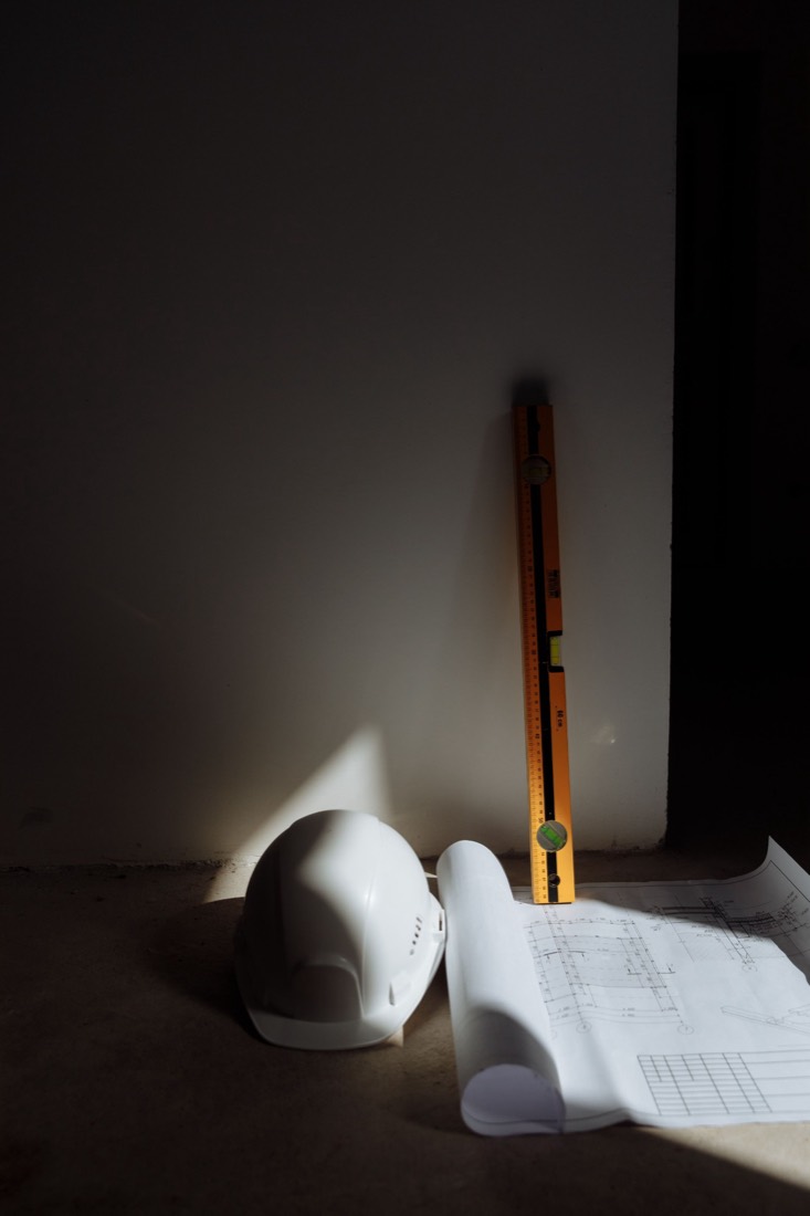Casque, niveau à bulle et plan roulé posés sur le sol d’un chantier